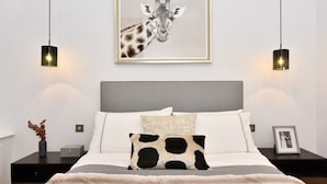A bedroom with a bed, two bedside tables, a framed giraffe picture, and pendant lights. - Albemarle Elegance I - 37as1 (London)