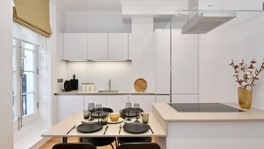 A modern kitchen with white cabinetry, a dining table set with black plates, glasses, and cutlery, and a vase with flowers on the countertop. - Albemarle Elegance I - 37as1 (London)