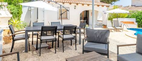 Eine Außenpatio mit Pool, umgeben von einem weißen Gebäude mit Ziegeldach, ausgestattet mit Tischen, Stühlen und Sonnenschirmen.