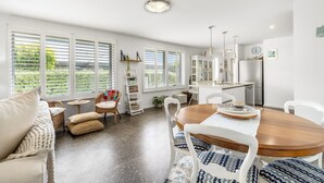 Un amplio salón con una mesa de comedor de madera, sillas blancas y un gran ventanal con persianas.