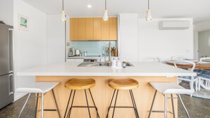 Una cocina moderna con encimeras blancas, taburetes de madera e iluminación colgante.