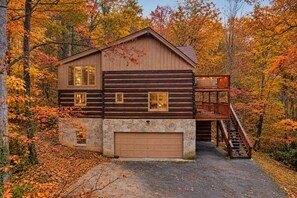 A log cabin with a stone foundation, a garage, and a wooden deck with a staircase.
