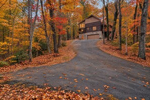 A two-story log cabin with a stone foundation, surrounded by a forest with autumn foliage.