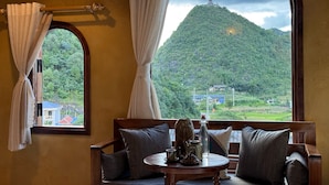 A room with a view of a mountain, a flag, and a table with a bottle and teapot.