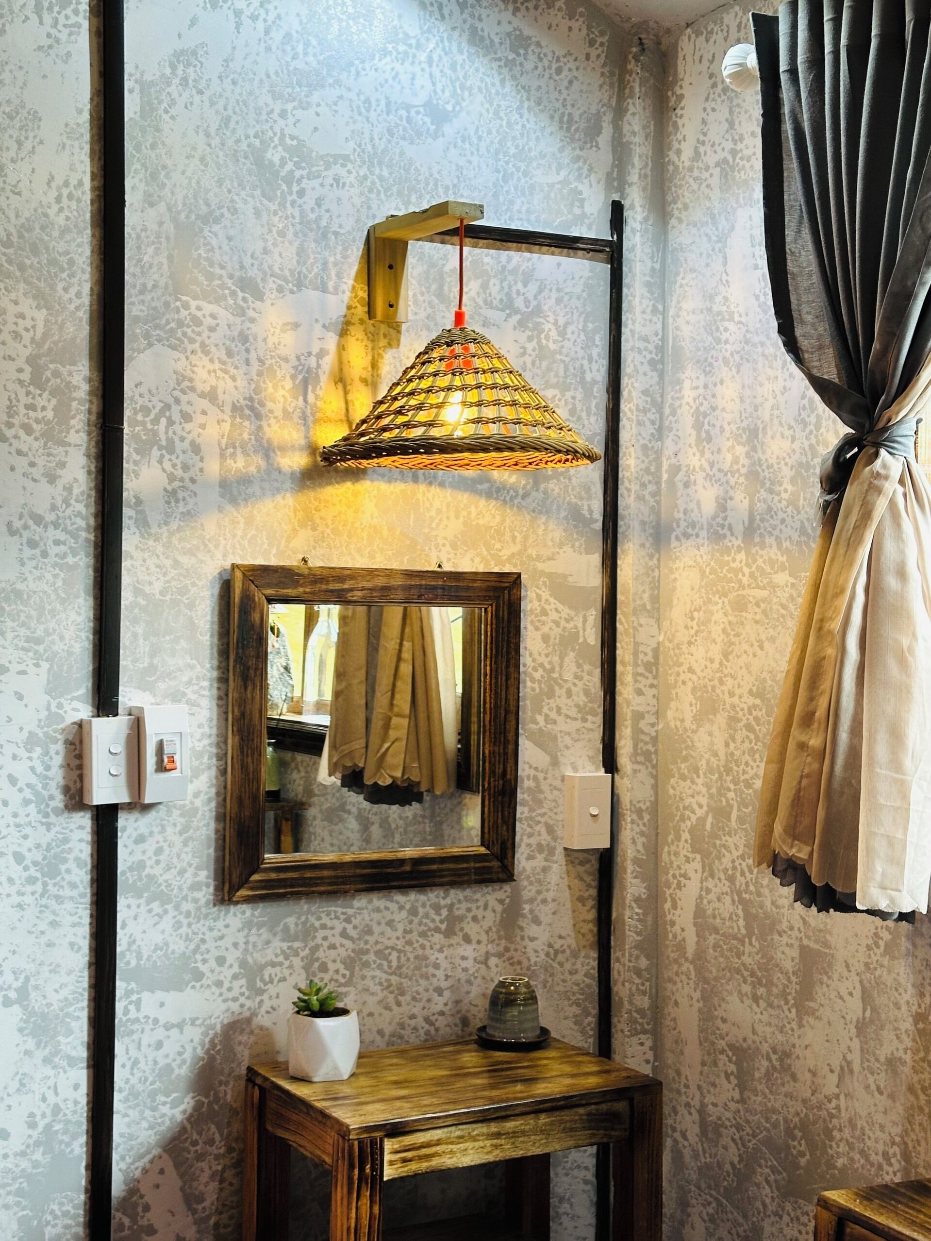 A room with a textured wall, a hanging lamp, a mirror, a small table with a plant, and a curtain.