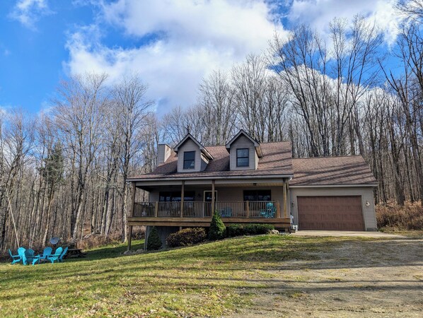 A two-story house with a front porch, a garage, and a wooded backdrop.