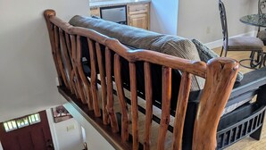 Uma escadaria de madeira com um banco acolchoado no topo, que leva a um quarto com uma cama e uma pequena mesa.