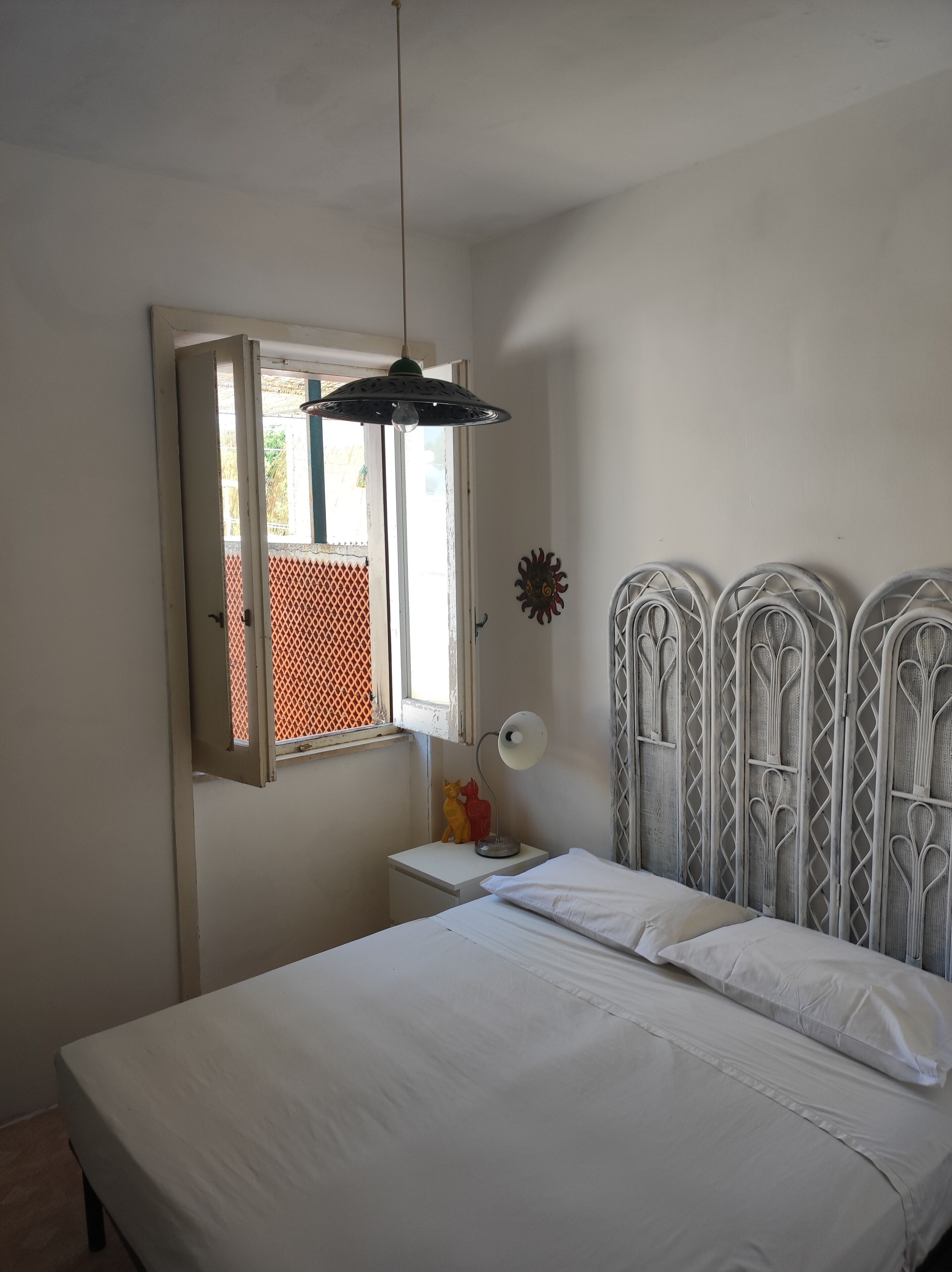 Un dormitorio con cama, mesita de noche con lámpara, ventana con vistas y un adorno decorativo en la pared.