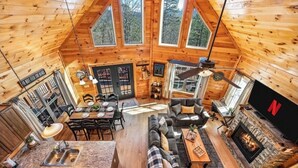 A cozy log cabin interior with a dining area, living room, fireplace, and large windows. - Firefly Ridge! Cozy, Fishing Pond, Hot Tub, Fire Pit! (Sevierville)