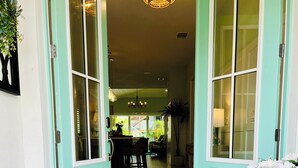 Une porte de couleur turquoise donne accès à une pièce agrémentée d’un lustre, d’un coin repas et d’un tapis sur lequel est inscrit un message.