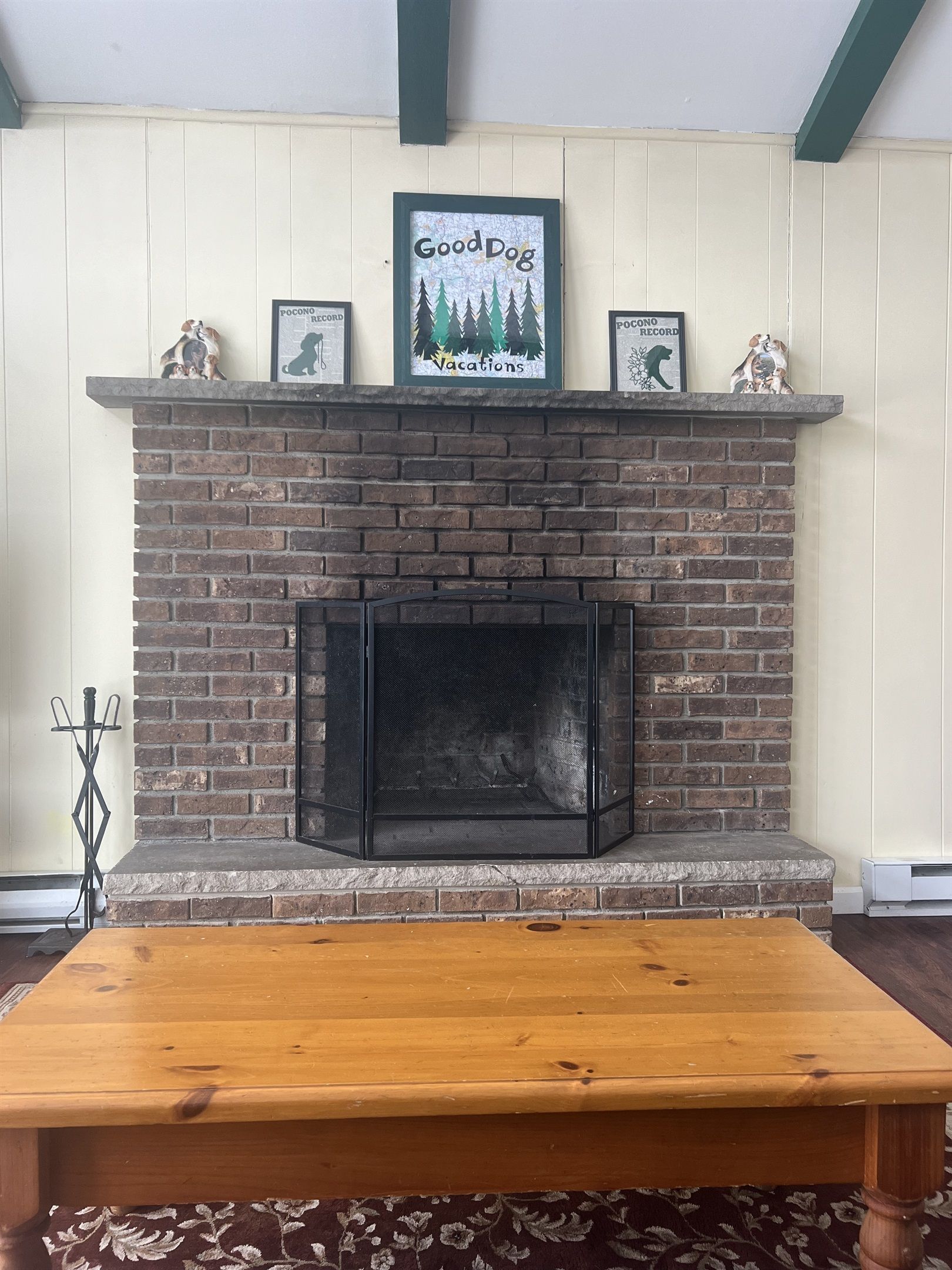 A brick fireplace with a mantel displaying framed pictures and a sign that reads 'Good Dog Vacations.'