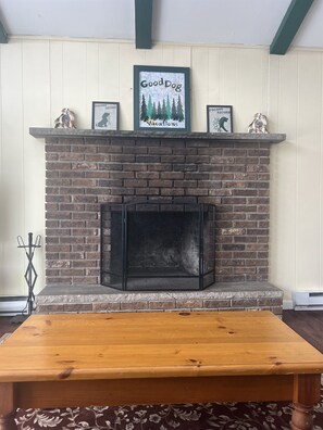 A brick fireplace with a mantel displaying framed pictures and a sign that reads 'Good Dog Vacations.'