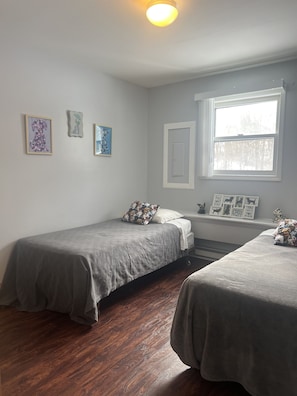 Ein Zimmer mit zwei Betten, einem Fenster und Wandbildern.