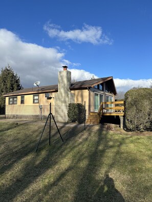 Una casa moderna de dos pisos con una chimenea grande, una terraza y un patio cercado.