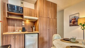 A compact kitchen with wooden cabinets, a microwave, a small refrigerator, and a dining area with a table set for two. - La Suite Yak - Très beau studio - Charpennes-Tonkin (Villeurbanne)