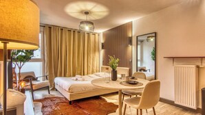A modern hotel room with a large bed, a round dining table, a chair, a lamp, a mirror, and a radiator. - La Suite Yak - Très beau studio - Charpennes-Tonkin (Villeurbanne)