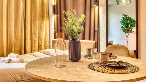 A hotel room with a bed, a round table with a vase and glass, and a plant. - La Suite Yak - Très beau studio - Charpennes-Tonkin (Villeurbanne)