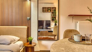 A modern room with a bed, a small table with a cup and glass, a mirror reflecting a kitchen area, and a radiator. - La Suite Yak - Très beau studio - Charpennes-Tonkin (Villeurbanne)