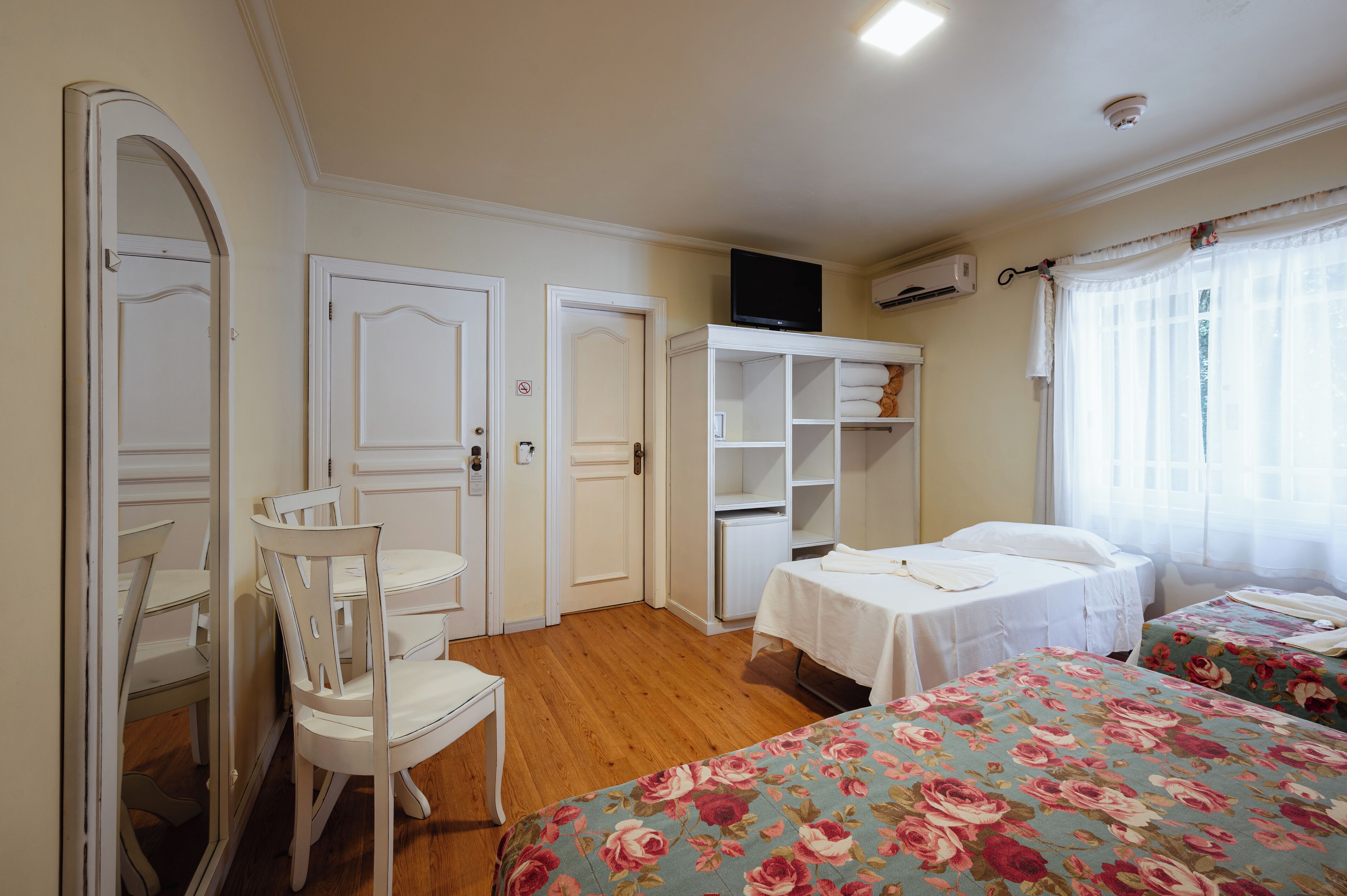 A bedroom with two beds, a dining table, chairs, a TV, and a wardrobe.