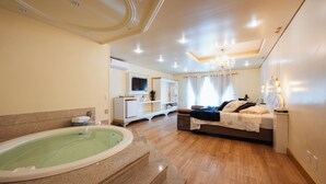 A spacious bedroom with a large bed, a sitting area, a built-in TV, and a bathtub. - Pousada dos Anjos (Canela)