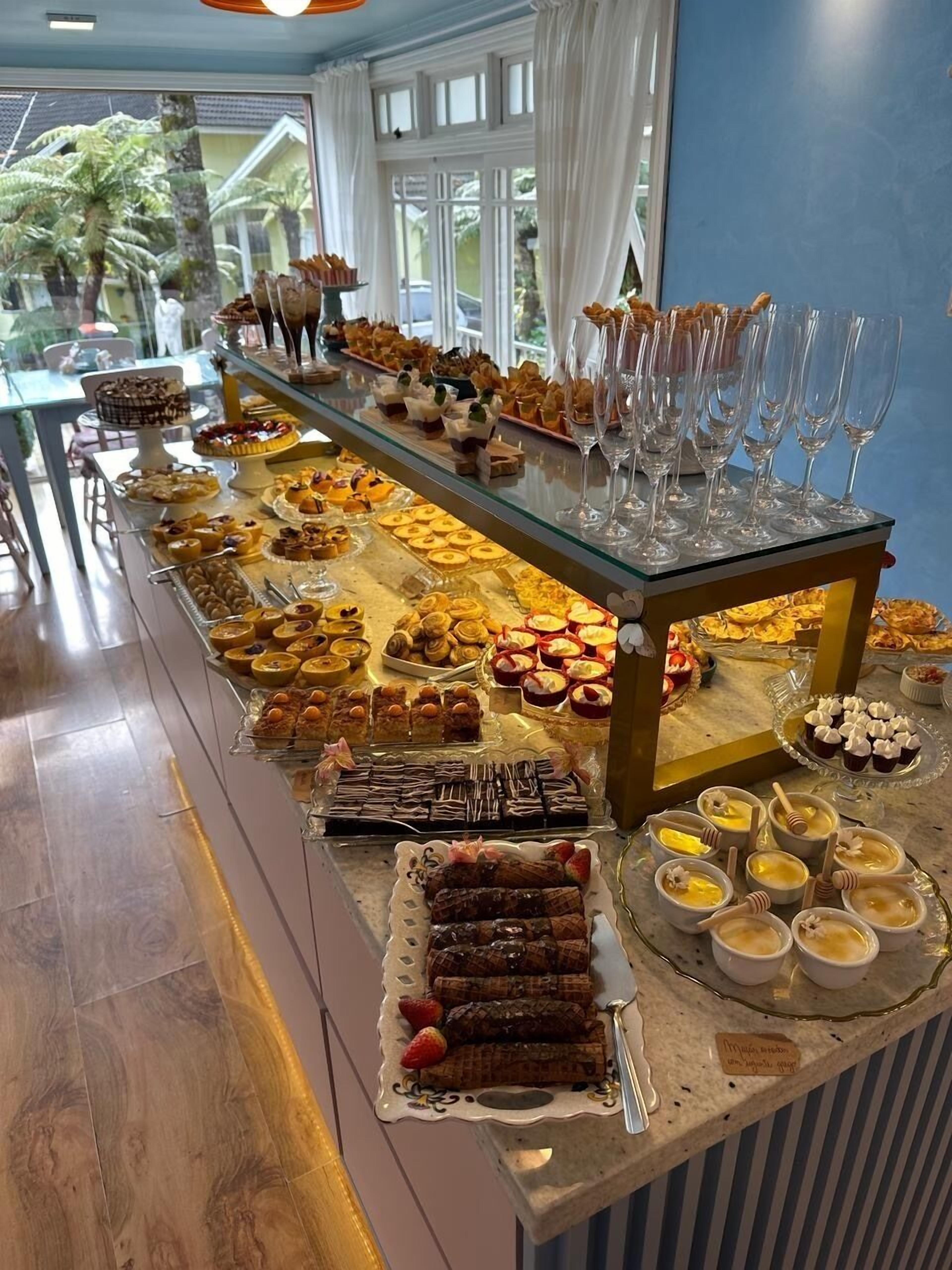 Monipuolinen buffet, jossa on tarjolla erilaisia jälkiruokia ja juomia, lasivitriini ja näkymä ulos.