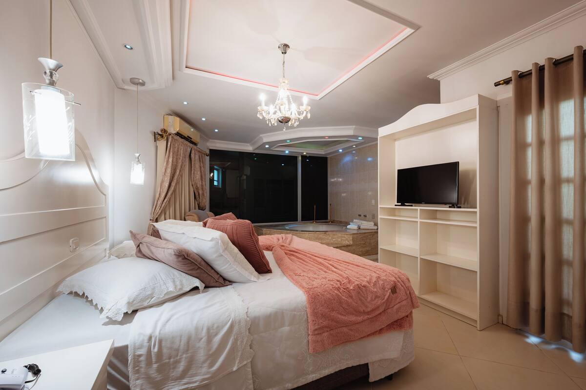 A modern bedroom with a large bed, a TV, and a bathroom with a bathtub.