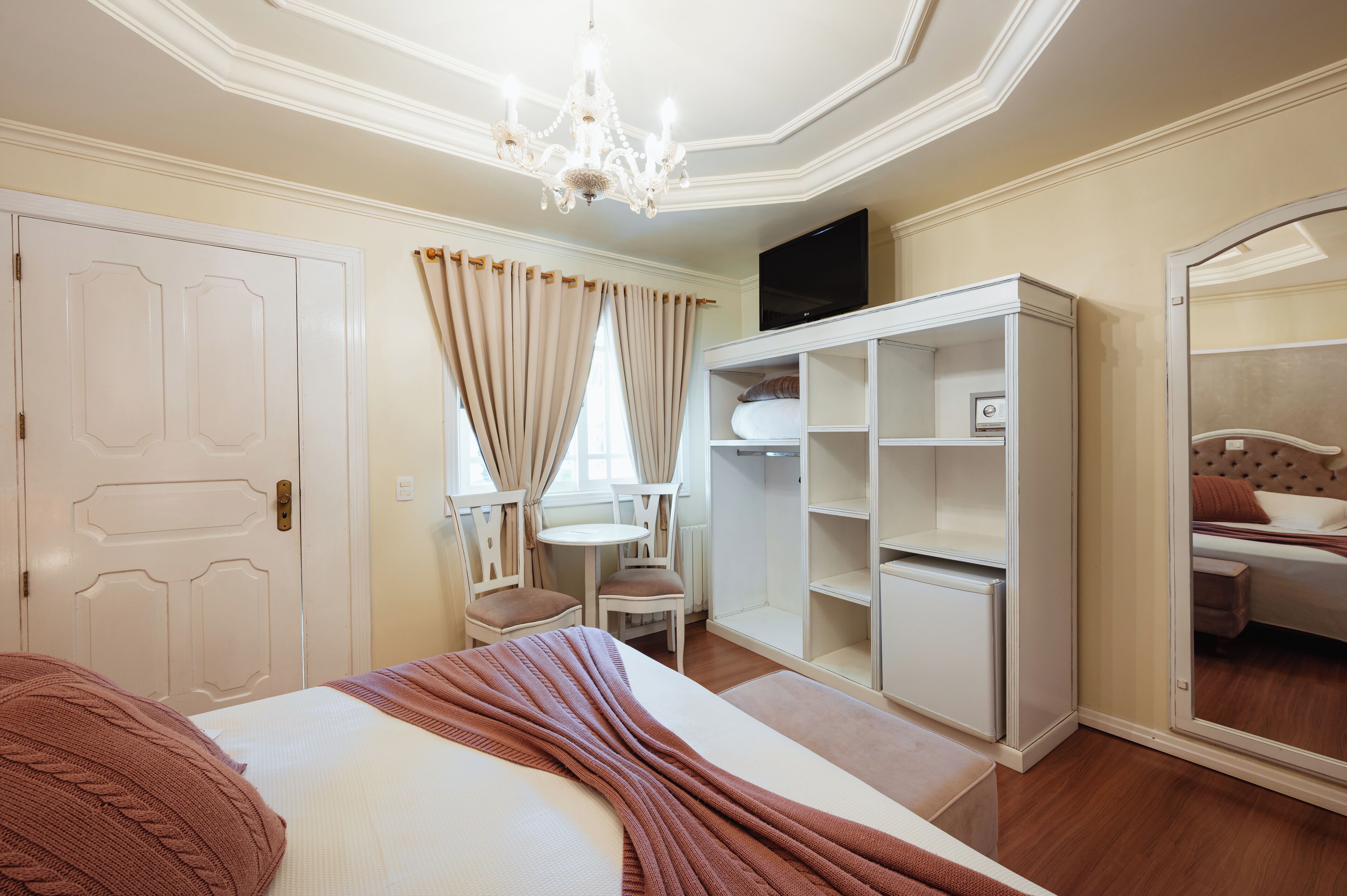 Una habitación de hotel con cama, tocador con espejo, armario y televisor.