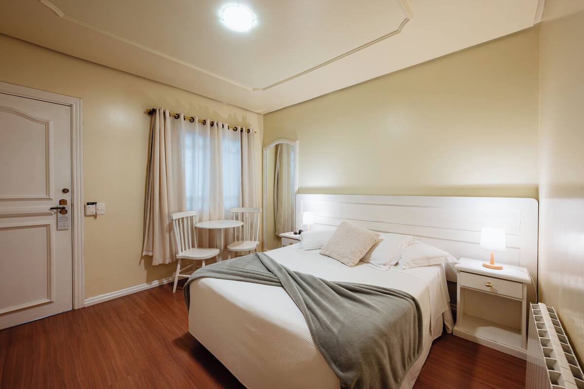 A neatly arranged bedroom with a bed, bedside tables, a nightstand, a chair, and a small table.