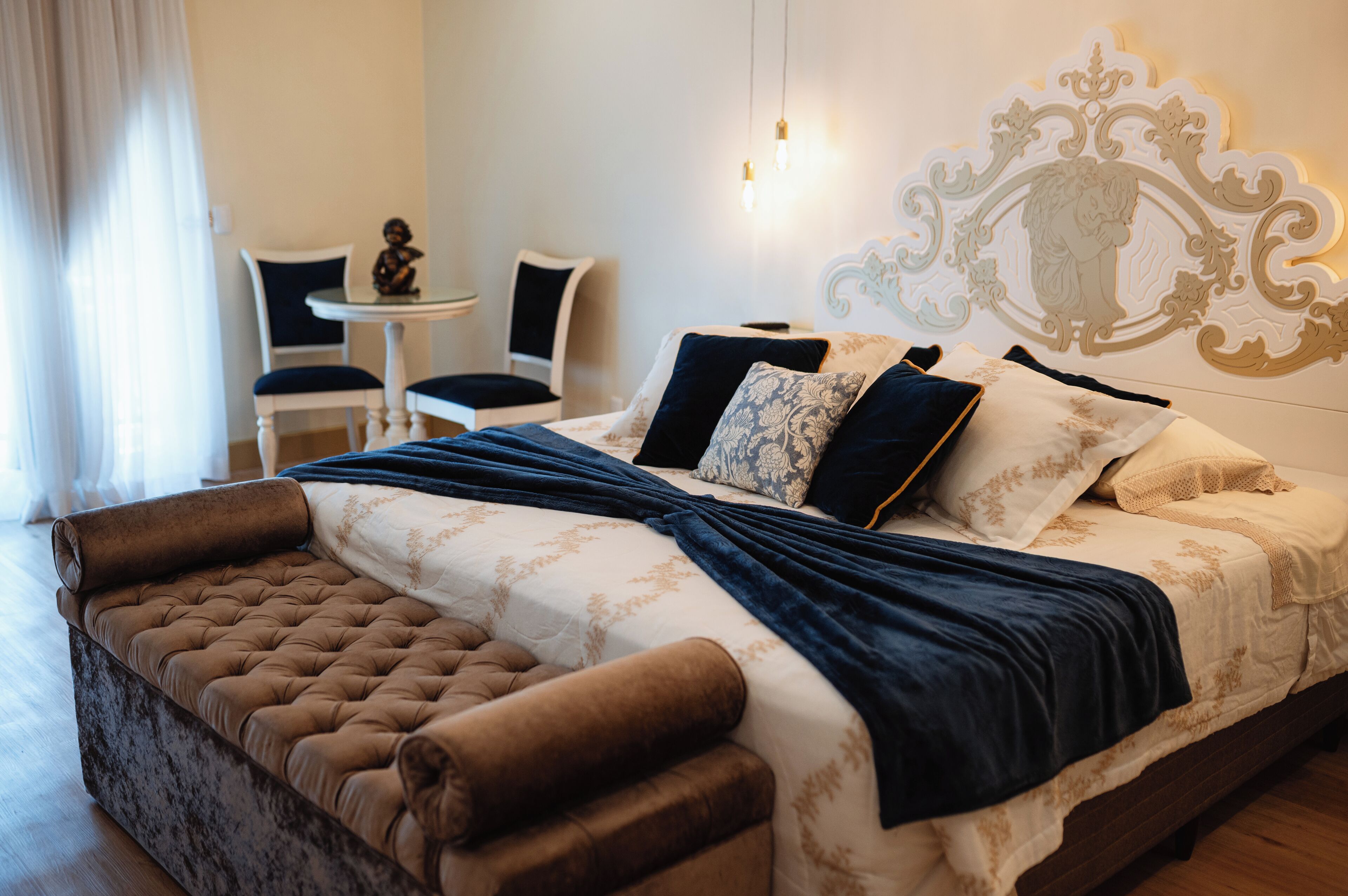 A bedroom with a large bed, a small table, two chairs, and a decorative wall piece.