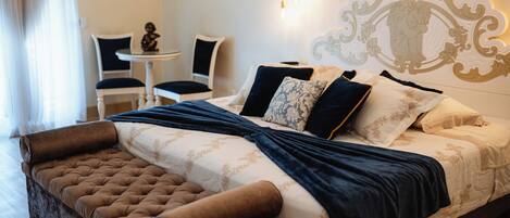 A bedroom with a large bed, a small table, two chairs, and a decorative wall piece.