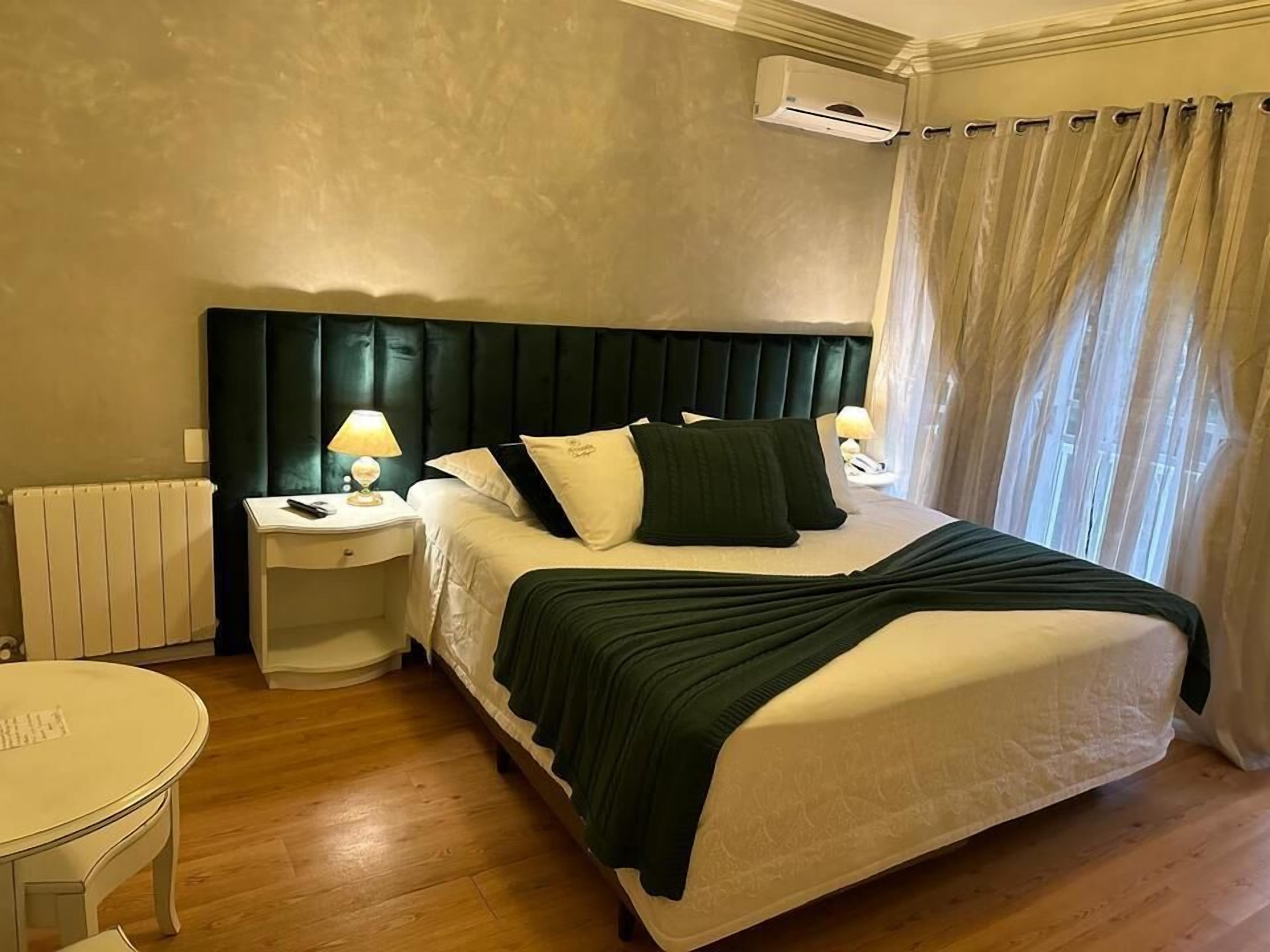 Een hotelkamer met een bed, nachtkastjes, een lamp, een radiator en een raam met gordijnen.