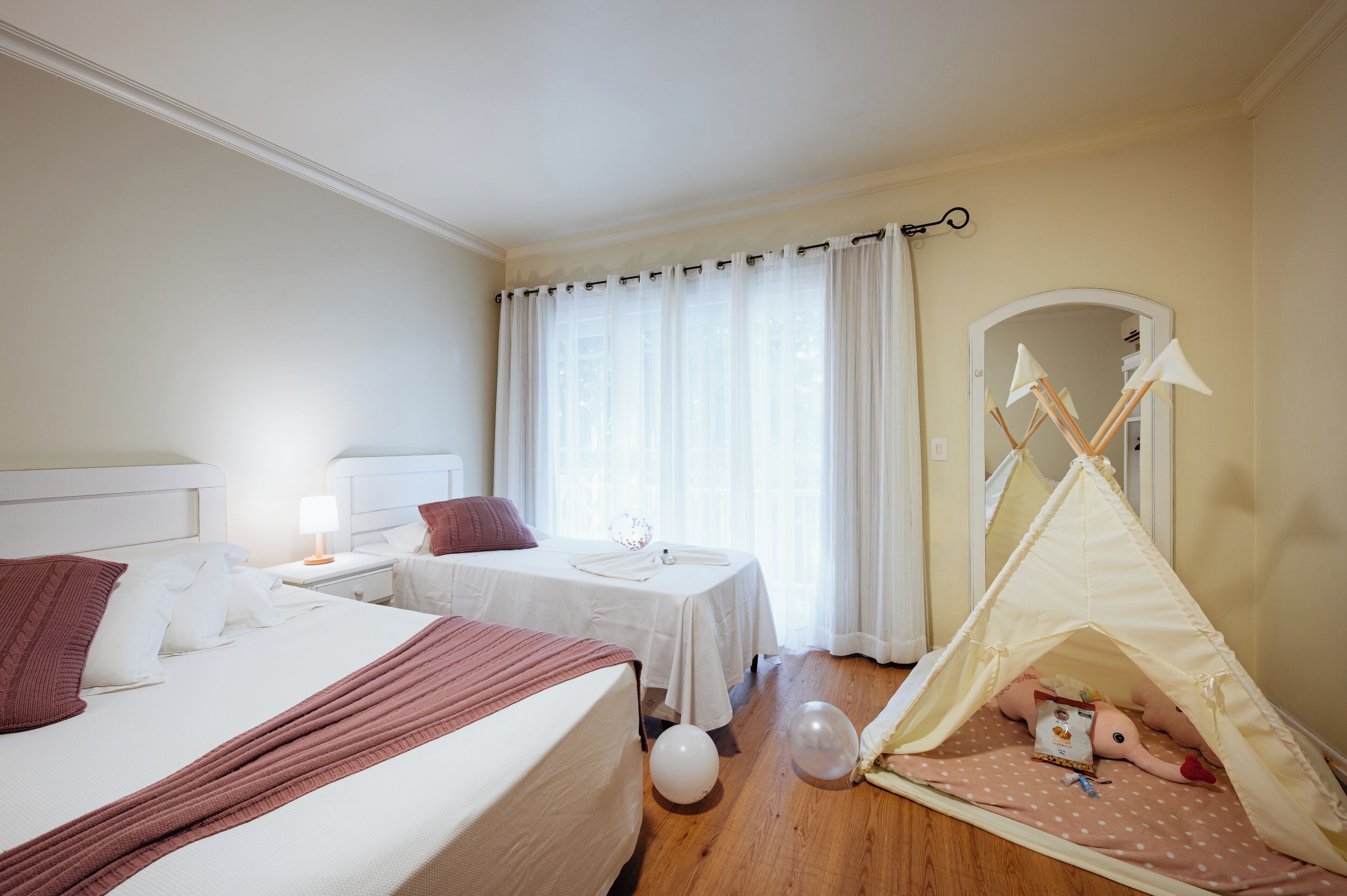 A hotel room with a large bed, a smaller bed, a tent, and a window with curtains.
