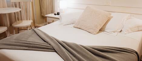 A neatly made bed with a white headboard, a brown throw blanket, and a bedside table with a lamp and a phone.