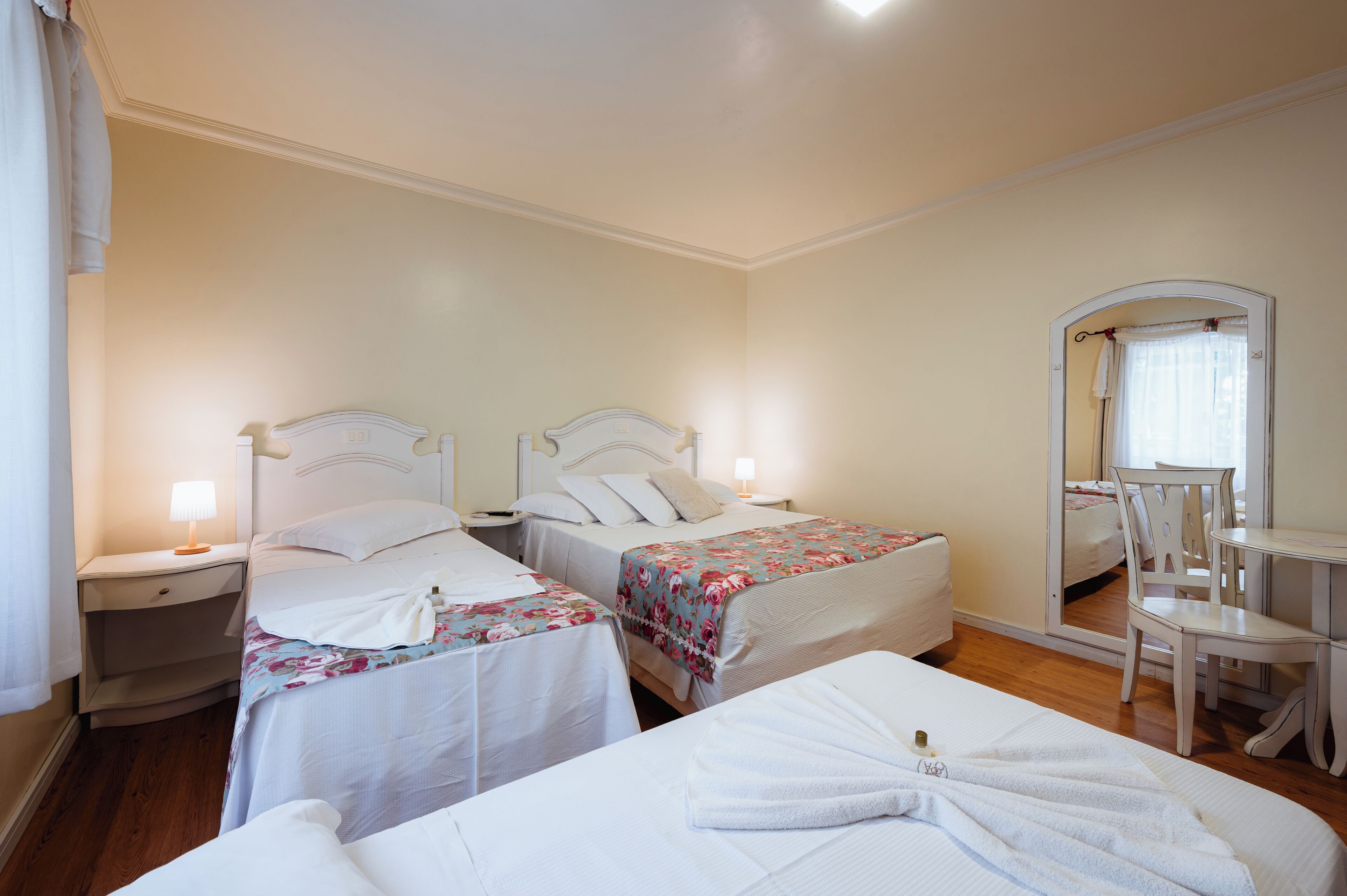 A hotel room with two beds, a small table, a chair, and a mirror.