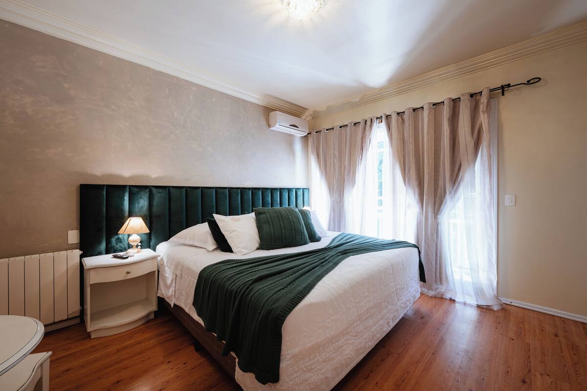 A bedroom with a bed, bedside table, lamp, and curtains.