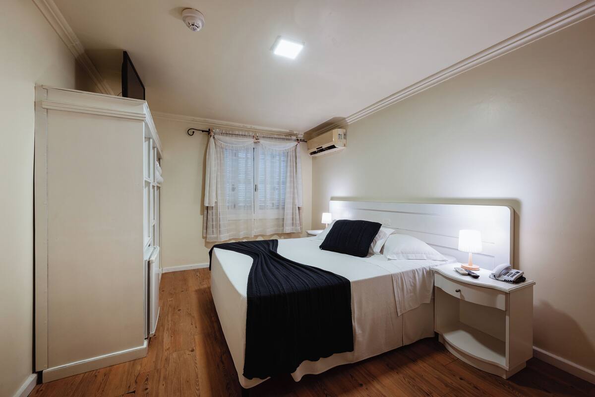 A bedroom with a bed, bedside table, lamp, and an air conditioning unit.