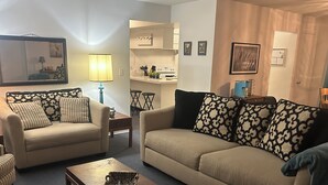 A living room with two sofas, a coffee table, and a kitchen area in the background. - Charming 3-bedroom house with lake views in serene Spring Hill (Spring Hill)