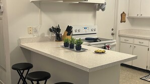 A kitchen with a central island, four stools, a stove, and a clock on the wall. - Charming 3-bedroom house with lake views in serene Spring Hill (Spring Hill)