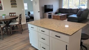 A modern kitchen with a granite countertop, white cabinetry, and a dining area with a round table and chairs. -  Lake Tillery Area, 4-bedroom house in charming Norwood with WiFi, Deck and AC (Norwood)