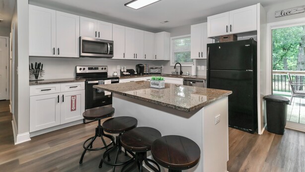 A modern kitchen with white cabinets, a central island with stools, a black refrigerator, and a microwave. -  Lake Tillery Area, 4-bedroom house in charming Norwood with WiFi, Deck and AC (Norwood)