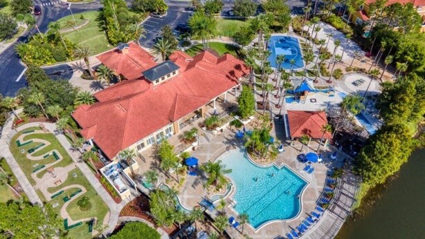 Vista aérea de un complejo turístico con piscina, canchas de tenis y un edificio grande con techo rojo.