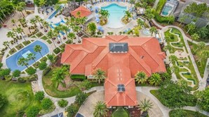 Vista aérea de un complejo turístico con un edificio central, varias piscinas y zonas ajardinadas.