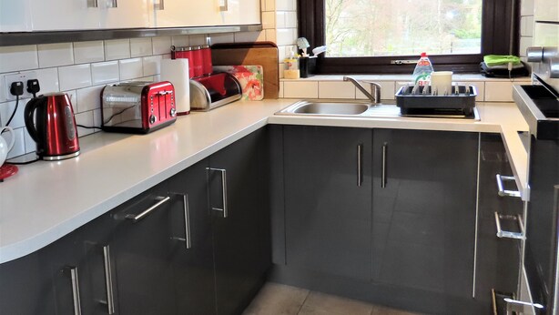 Een moderne keuken met donkere kastjes, een wit aanrecht en roestvrijstalen apparatuur, waaronder een broodrooster, waterkoker en blender.