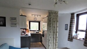 Een woonkamer met een bank, een salontafel, en een keukenhoek met een raam en gordijnen.