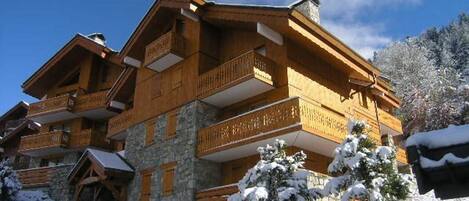 A multi-story wooden chalet with balconies, stone walls, and a snowy landscape.