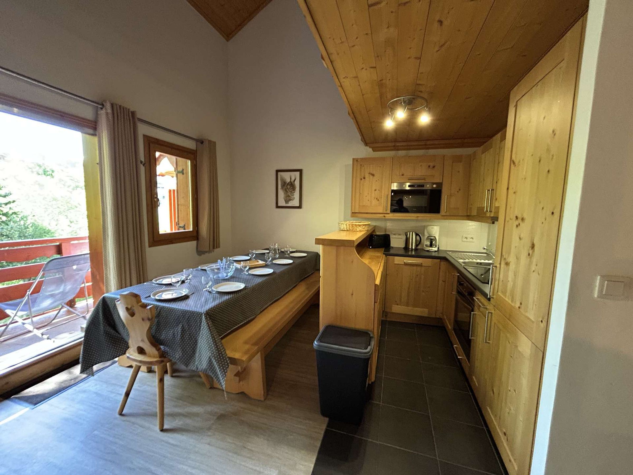 A compact kitchen with wooden cabinets, a dining table set for four, and a view of the outdoors.