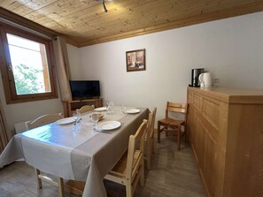 Uma área de refeições com mesa posta para quatro pessoas, uma televisão e uma cafeteira em uma bancada de madeira.