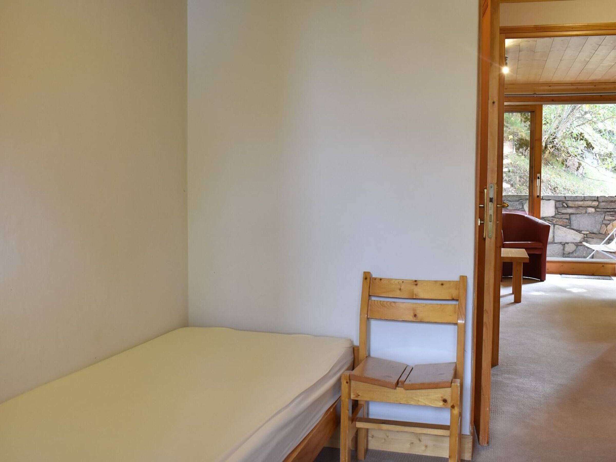 Una habitación pequeña con cama individual, una silla de madera y un banco.