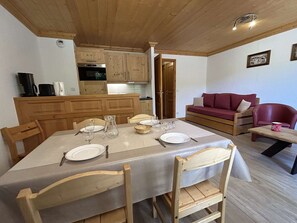 A dining area with a table set for four, wooden chairs, a kitchen with wooden cabinets, a red sofa, and a red armchair. - 2-room apartment in Méribel with parking near ski (Méribel)