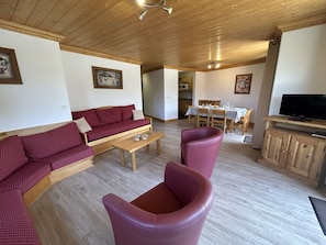 Ett vardagsrum med en soffa, ett soffbord och stolar, en matplats med ett bord och stolar samt en tv som står på ett träskåp.